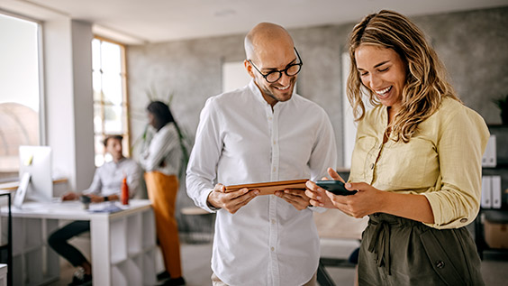 image of cheerful and smiling young successful female businesswoman standing with colleague looking at smartphone in modern office and coworking space.